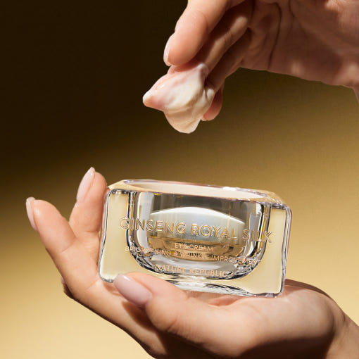 AgelessBeauty3000.com NATURE REPUBLIC | Ginseng Royal Silk Eye Cream Crimson Peak Ginseng Royal Silk eye cream in clear packaging held by a hand against a gold background