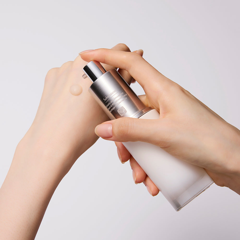 AgelessBeauty3000.com  Sulwhasoo | The Ultimate S Serum  Two hands holding a silver and white skincare bottle against a light gray background