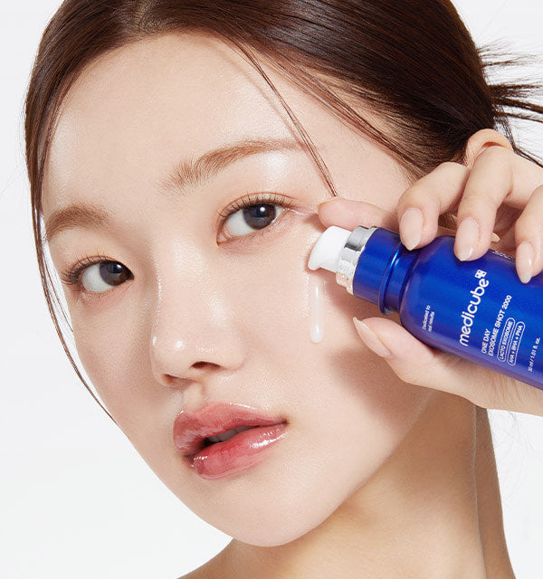 AgelessBeauty3000.com  medicube |One Day Exosome Shot Pore Ampoule 2000 Woman applying a blue bottle of Medicube product to her face.