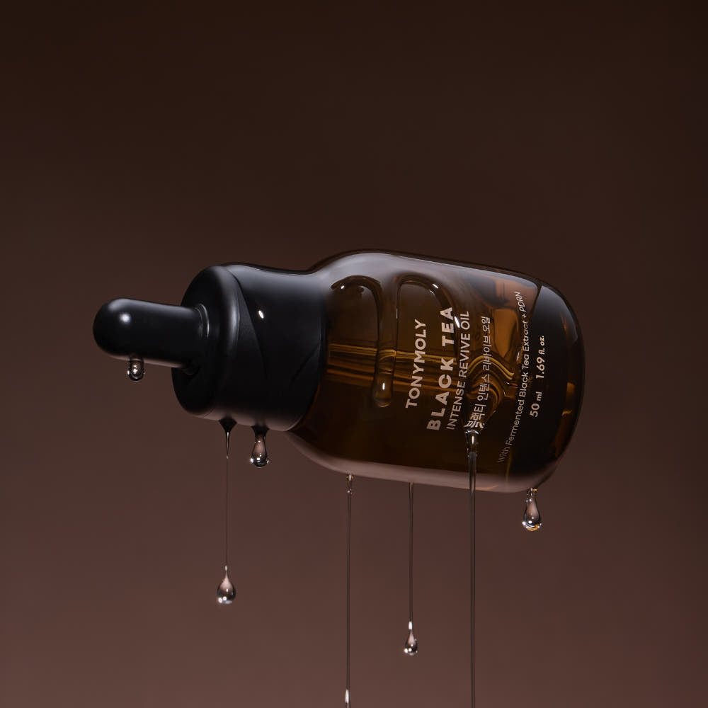 AgelessBeauty3000.com  Bottle of Tony Moly Black Tea Renew Revive Oil with droplets on a brown background