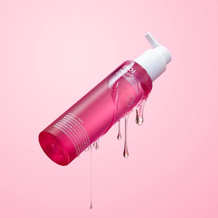 AgelessBeauty3000.com  isoi  | Brightening Cleansing Oil Pink skincare bottle with droplets on a pink background